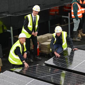 Two men crouch next to solar panels, with a third standing in the centre